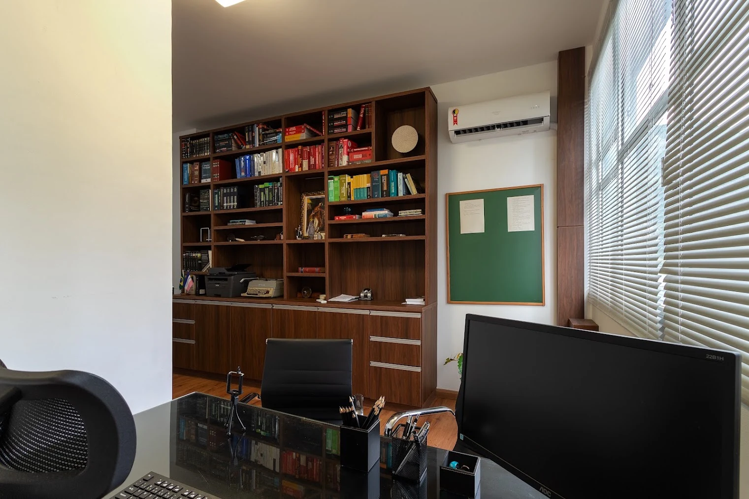Sala de atendimento do escritório, com mesa e biblioteca.
